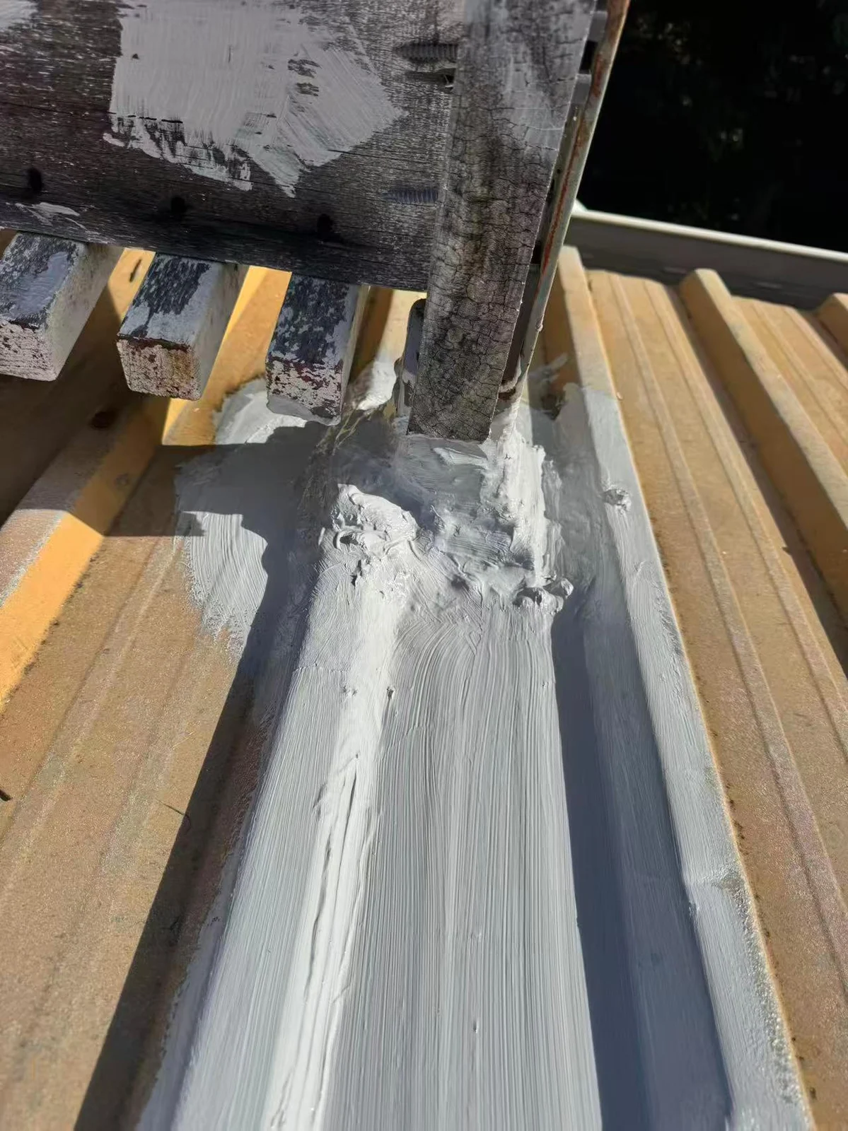 Grey coating extending along the metal roof beneath a timber post
