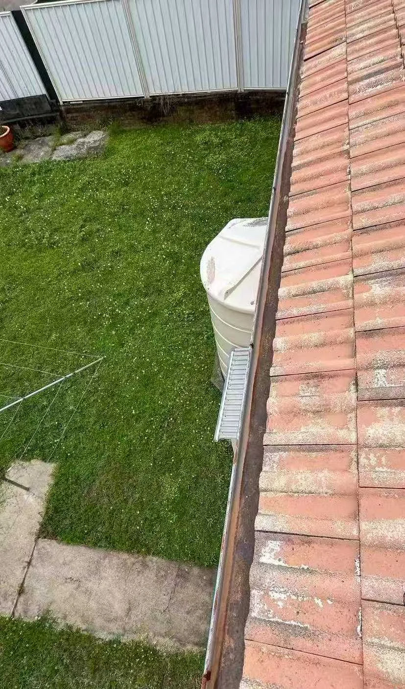 Cleared gutter beside a tiled roof after leaves and debris were removed